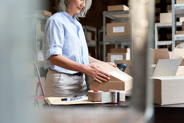 Close up over shoulder view of old female online store small business owner worker packing package...