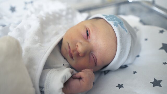 Adorable newborn baby sleeping peacefully in his crib in the hospital room . High quality photo