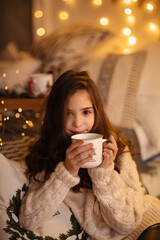 Beautiful little dark-haired girl in the studio with New Year's decor and confetti. The child is having fun and playing. Portrait of a child. The child sits near the bed and holds a cup