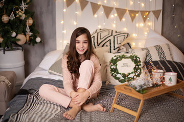 Beautiful little dark-haired girl in the studio with New Year's decor and confetti. The child is having fun and playing. Portrait of a child. The child sits on the bed near the Christmas tree