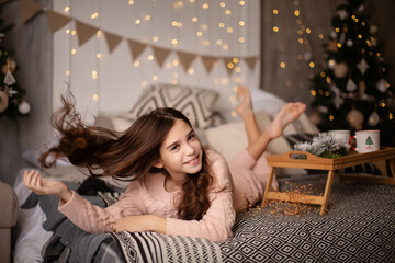 Beautiful little dark-haired girl in the studio with New Year's decor and confetti. The child is having fun and playing. Portrait of a child. The child lying on the bed near the Christmas tree