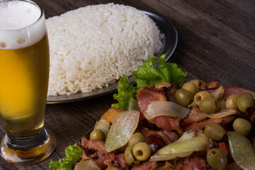 Fried chicken with rustic onions and bacon, accompanied by a refreshing glass of beer and white rice. Brazillian tipical food. Gourmet close-up horizontal photography.