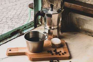 Italian lack coffee in a cup with coffee beans and a handmade cookie with sugar and a moka pot behind. Everything in vintage brown background close to the window.