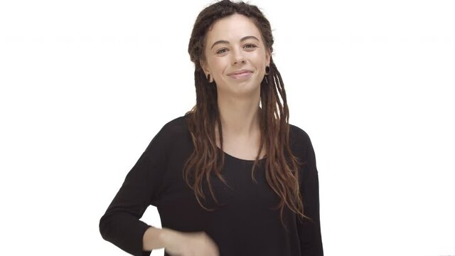 Video of attractive modern girl with dreadlocks and ear tunnels, wearing black blouse, saying hello and friendly waving hand at camera, greeting someone, standing over white background