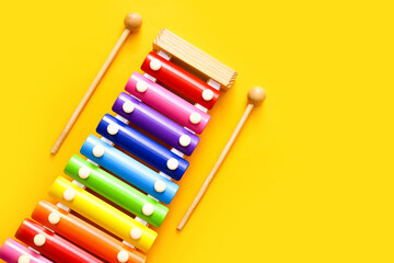 Rainbow colored toy xylophone with two sticks on yellow background. Copy space
