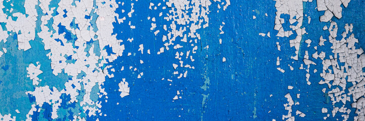 Peeling paint on the wall. Panorama of a concrete wall with old cracked flaking paint. Weathered rough painted surface with patterns of cracks and peeling. Wide panoramic grunge texture for background