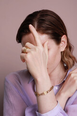 Fototapeta premium Vertical portrait of caucasian woman closed her face with hand, wearing lila blouse, posing over light pink background.