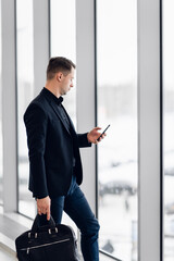 Business man using mobile phone app in airport. Young business professional man texting smartphone walking inside office building or airport terminal. Handsome man wearing stylish suit jacket indoors.