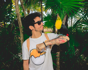 Happy tattooed young guy with sunglasses with a toucan paradise bird in a jungle