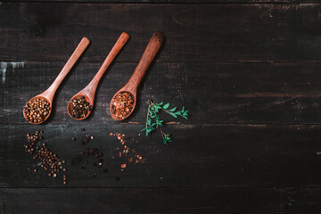 various seasonings on wooden spoons, coriander, chili powder, pepper and oregano, on dark rustic background