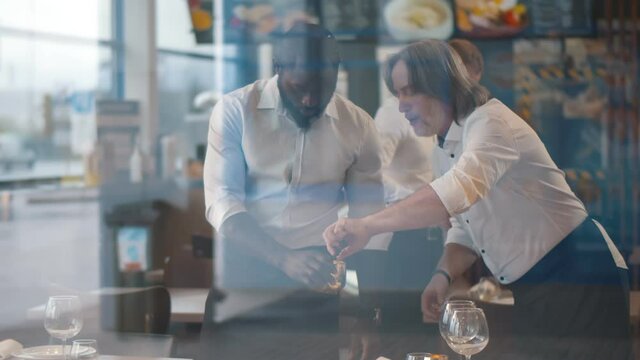 View through window of diverse waiters in uniform serving tables in restaurant