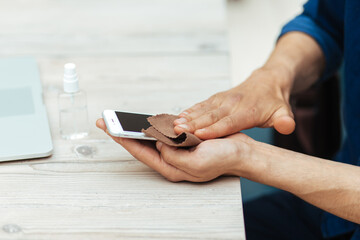 close up. a young man in a protective mask wiping the screen of his smartphone.