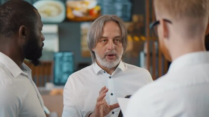 Male restaurant manager with digital tablet giving team talk to waiting staff