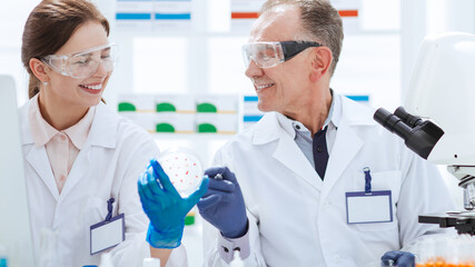 smiling scientists with a Petri dish sitting at a laboratory table.