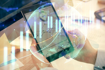 Double exposure of man's hands holding and using a phone and financial graph drawing. Analysis concept.