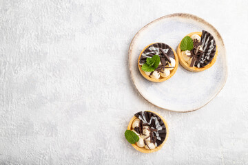 Sweet tartlets with chocolate and cheese cream on a gray concrete background, flat lay, copy space.