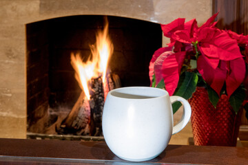 a cup of coffee on a table by a roaring fireplace with a poinsettia for Christmas