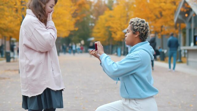 Side view of african woman proposing to her happy caucasian girlfriend outdoors