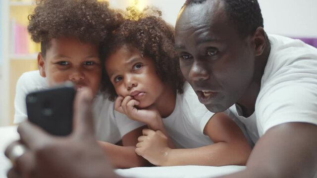 Happy african american father with little son and daughter taking selfie on smartphone at home