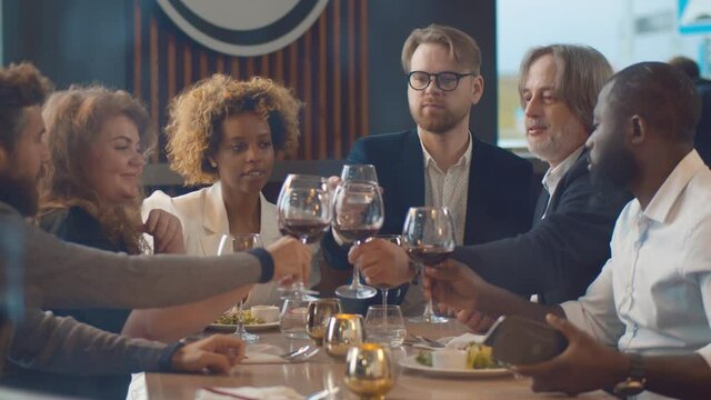 Group of diverse people enjoying dinner together and cheers with wine glasses