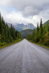 View of Scenic Road surrounded by Trees and Mountains on a Cloudy Fall Morning in Canadian Nature. Taken in Northern British Columbia, Canada.