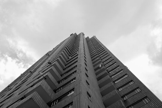 Low Angle View Of A Brick Symmetrical Skyscraper Corner With Cloudy Sky At Background. Black And White Photography