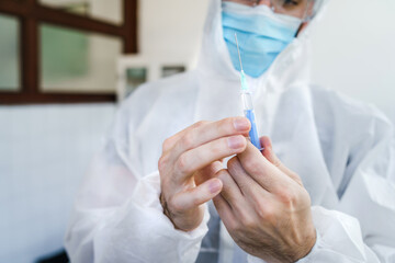 Close up on hands of male surgeon or doctor in protective suit holding injection of medicine or vaccine at hospital taking the dose - healthcare covid-19 concept selective focus