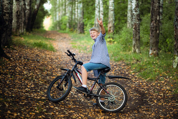 Fototapeta na wymiar Joyful boy on a bicycle with a hands raised in the park
