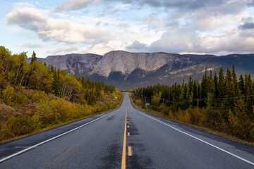 View of Scenic Road surrounded by Trees and Rocky Mountains on a Cloudy Fall Day in Canadian Nature. Taken near Whitehorse, Yukon, Canada.