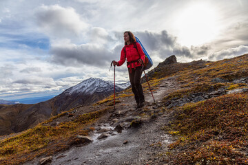 Obraz premium Woman Backpacking along Scenic Hiking Trail surrounded by Mountains in Canadian Nature. Season change from Fall to Winter. Taken in Tombstone Territorial Park, Yukon, Canada.