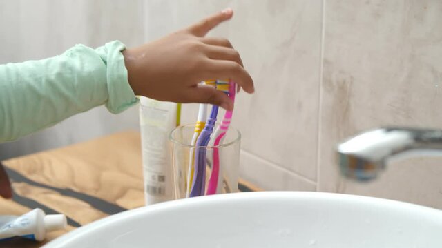 Close up of african kid and parent squeezing toothpaste on toothbrush cleaning teeth in bathroom