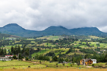Cloudy Landscape with mountains, cows, houses and green trees between them, taken from  another...