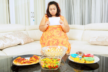 Obraz na płótnie Canvas Unhappy fat woman hold blank paper near junk foods