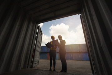 two engineer worker hold a laptop, document for checking a quality of containers box from cargo ship for export and import, blue container background