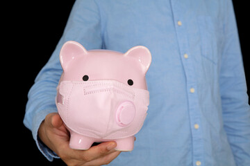 A man holding a piggy bank wearing a mask in front of a black background