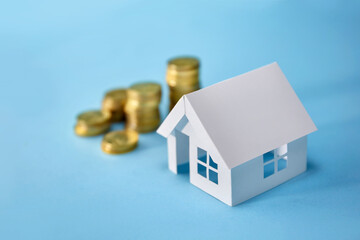 Paper house model and coin money on blue background