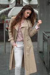 young latin woman with long wavy hair, standing in the city, wearing a coat, shirt and white pants, stylish style on the day