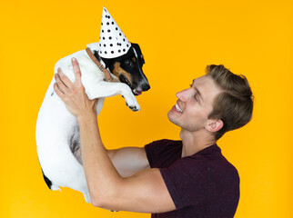man of European appearance on a yellow background. holding a dog jack russell looking at each other