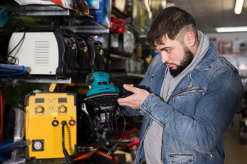 Fototapeta na wymiar Confident man choosing electric vibratory surface grinder in tools store