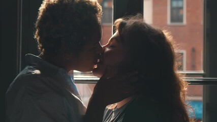 Couple of excited multiethnic lesbians kissing passionately in front of window