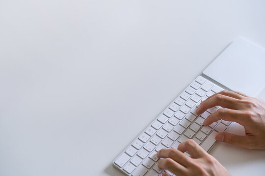 Man typing on the  modern wireless keyboard and trackpad on the desk. Office and working space has benn arranged in minimal modern style.