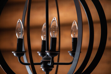 Black chandelier with old style candle lightbulbs with wooden log background in cabin, cottage.  