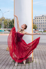 Woman ballerina in red ballet dress dancing in pointe shoes next to the old columns