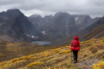 Woman Backpacking on Scenic Hiking Trail to Lake surrounded by Mountains during Fall in Canadian Nature. Taken in Tombstone Territorial Park, Yukon, Canada.