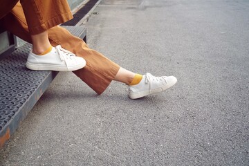 Side Part of human. Low section. person sitting on a step wearing in brown trouser and white sneaker. Street or hipster style.