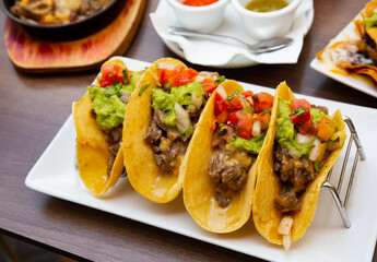 Mexican tacos with beef, guacamole and vegetables at plate