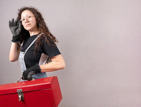 Mujer constructora con overol sosteniendo una caja de herramientas met&aacute;lica de color rojo con las manos usando guantes para construcci&oacute;n con copy space para texto publicitario