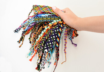 Obraz na płótnie Canvas Female hand holding many woven multi-colored DIY friendship bracelets handmade of embroidery thread with knots on white background.