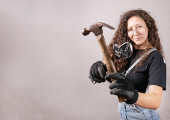 Mujer contratista joven posando con herramientas de construcción como martillo, llave inglesa y usando guantes . Plano medio con copyspace para texto publicitario