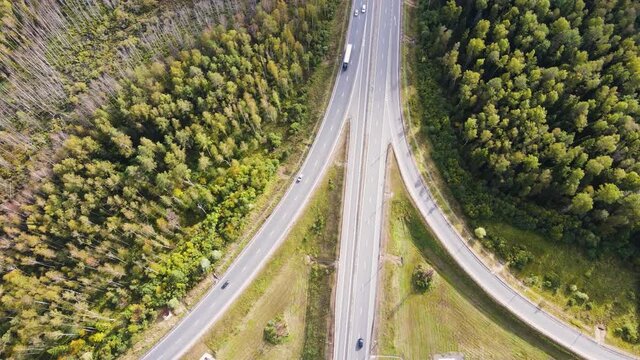Top view of a suburban road fork with cars. The vehicles travel slowly in different directions. There is a dense forest with green trees. Slow motion drone shooting. Warm summer day. Soft light. UHD.